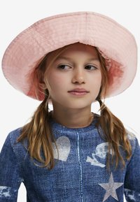 Ružový prešívaný klobúk so širokým okrajom, ktorý má textúrovanú látku. Subjekt má oblečený denimoový top so striebornými vzormi.