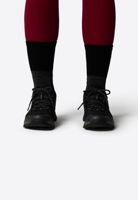 Black athletic shoes with textured mesh and synthetic overlays, laces, and rubber outsoles. Worn with dark crew-length socks and fitted leggings.