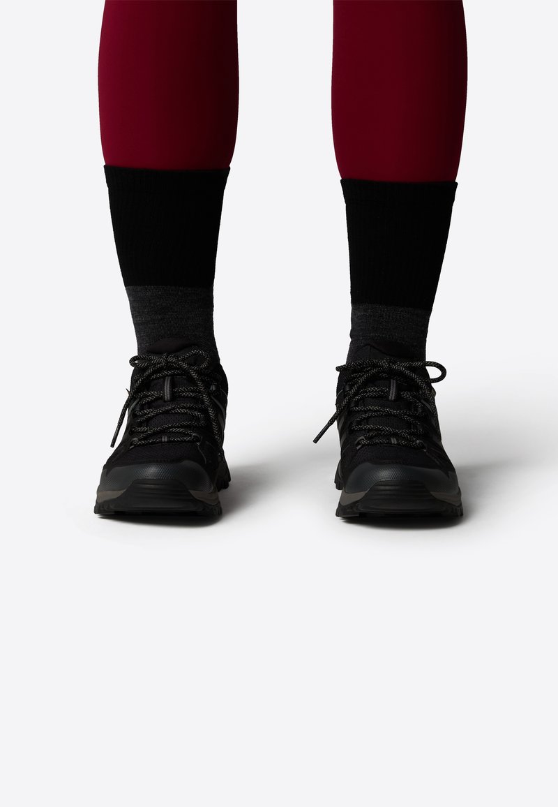Black athletic shoes with textured mesh and synthetic overlays, laces, and rubber outsoles. Worn with dark crew-length socks and fitted leggings.