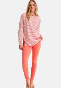 Haut à manches longues rayé rouge et blanc associé à un legging uni corail. Le tissu semble doux avec une coupe décontractée et des fentes latérales à l'ourlet.