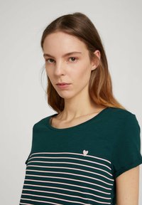 Maglietta a maniche corte verde scuro con strisce rosa orizzontali e un piccolo dettaglio a forma di cuore sul petto; realizzata in morbido cotone.