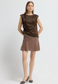 Brun satin top med draperet design, parret med en kort brun tweed nederdel med en plissering og accent hardware. Sorte stilethæle.