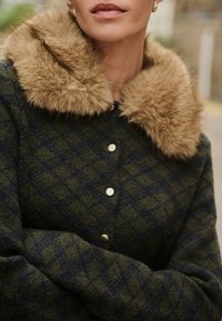 Cappotto a quadri verde e blu navy con colletto in pelliccia sintetica, caratterizzato da bottoni metallici e un aspetto di lana testurizzata.