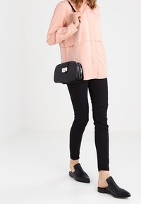 Černá crossbody taška se stříbrným řetízkovým popruhem, růžová dlouhá košile s dlouhým rukávem, černé skinny kalhoty a černé kožené slip-on boty.