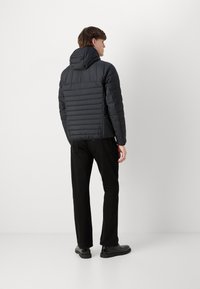 Svart puffjacka med huva, med kviltad textur och slankt mönster. Kombinerad med svarta byxor och svarta skor.