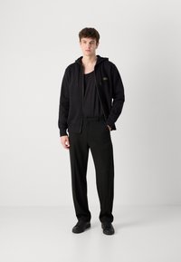 Black hoodie with zipper and adjustable drawstring, paired with black wide-leg trousers and black sneakers, featuring minimal design details.