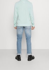 Maglione verde menta chiaro con polsini e orlo a costine, abbinato a jeans blu e scarpe nere, visto da dietro. Texture liscia.