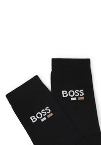 Calze nere in cotone con texture a coste, caratterizzate dal logo "BOSS" in bianco e marrone chiaro. Il design include accenti di colore a contrasto.