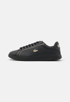 Baskets noires à profil bas avec fermeture à lacets à l'avant, logo latéral beige, accent beige au talon et texture lisse en cuir visible sur fond blanc.