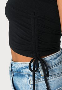 Top preto ajustado com laterais franzidas, apresentando uma bainha com cordão. Combinado com calções de ganga desgastados em azul claro.
