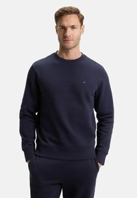 Sweat-shirt bleu marine en tissu doux avec un col rond, des poignets et une taille côtelés. Petit logo sur la poitrine. Texture lisse.