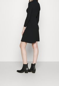 Robe tricotée noire à côtes, avec un col montant et des manches longues, présentant un ourlet évasé et associée à des bottines noires.