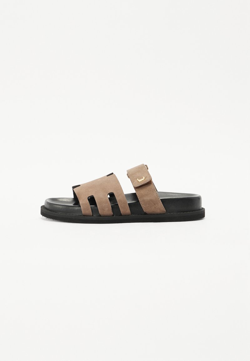 Suede glidesandal i brun og svart. Har to brede utskjæringer på overdelen og et justerbart belte med en gullspenne. Flat såle.