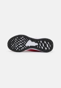 Suela de goma negra con patrón de agarre texturizado, parte superior de textil rojo con acentos blancos, que presenta un diseño elegante y soporte reforzado en el talón.