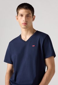 T-shirt bleu marine à col en V en coton, avec des manches courtes et un petit logo rouge Levi's sur la poitrine. Texture douce et design simple.