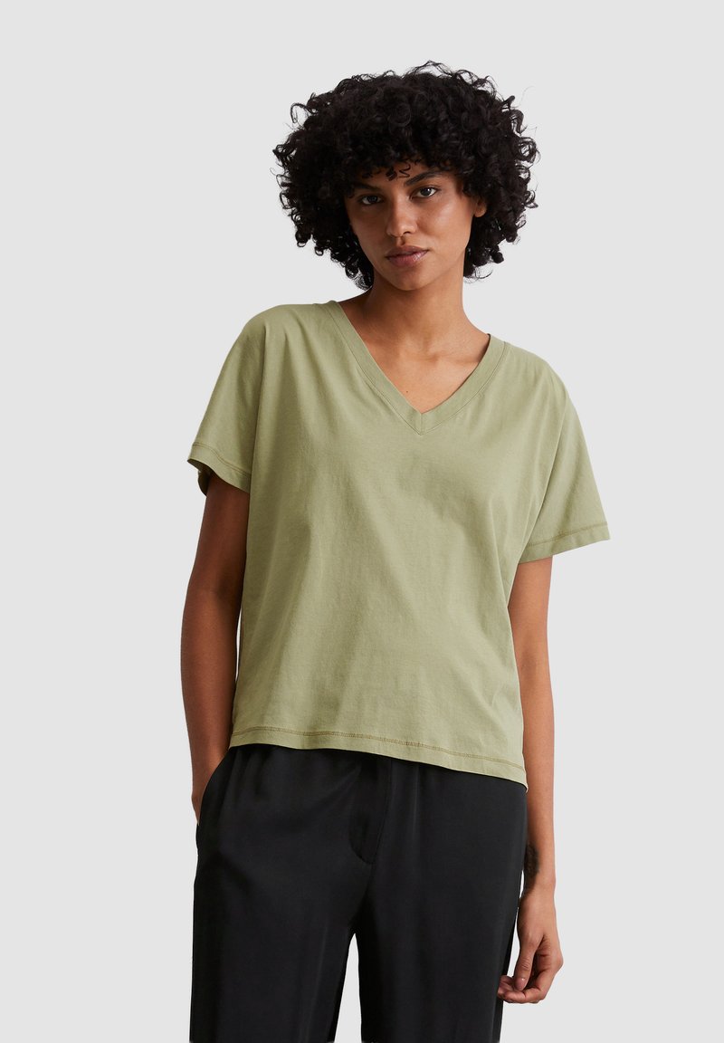 Jasnooliwkowa koszulka typu v-neck z krótkimi rękawami, wykonana z miękkiej bawełny; luźny krój oraz widoczne przeszycia na dolnym brzegu.