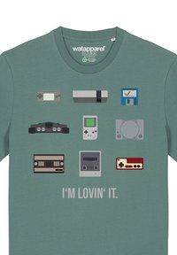 Green t-shirt featuring icons of various gaming consoles and controllers in gray and beige, along with the text “I’M LOVIN’ IT” at the bottom.