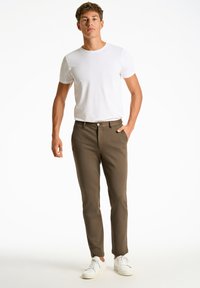 Vaaleanruskeat slim fit -housut, joissa on sileä pinta, vetskari ja napituskiristys sekä sivutaskut. Yhdistetty valkoisen t-paidan ja valkoisten lenkkareiden kanssa.