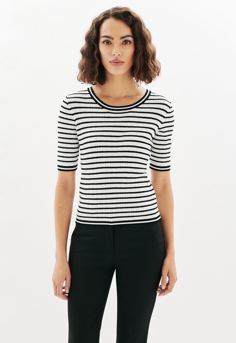 Top de punto de canalé a rayas en blanco y negro con mangas cortas y escote redondo, combinado con pantalones negros slim-fit.