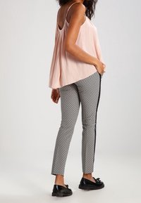 Lichtroze mouwloze top, gecombineerd met strakke zwart-wit gemusterde broek met zijstrepen en zwarte platte schoenen.