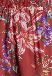 Tejido floral que presenta grandes lirios rosas y blancos con acentos morados sobre un fondo texturizado rojo-naranja, con cinturilla elástica.