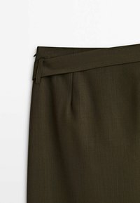 Tissu vert olive foncé avec une large ceinture et des passants pour ceinture sur un pantalon sur mesure.