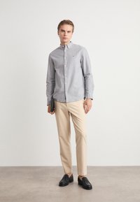 Ανοιχτό γκρι πουκάμισο με κουμπιά, μπεζ παντελόνια, μαύρες λιτές παπούτσια. Το πουκάμισο διαθέτει ένα μικρό λογότυπο στο στήθος, απαλό υφή και μακριά μανίκια.