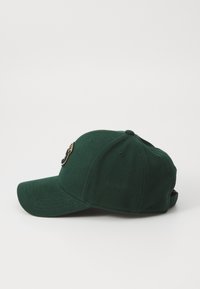 Grön basebollkeps i strukturerad tyg. Har en böjd skärm och en broderad logotyp framtill. Justerbart band baktill.