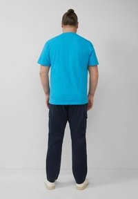 Türkises Rundhals-T-Shirt, figurbetontes Design, kombiniert mit navyblauen Cargo-Hosen mit Seitentaschen und elastischen Bündchen, getragen mit weißen Sneakern.