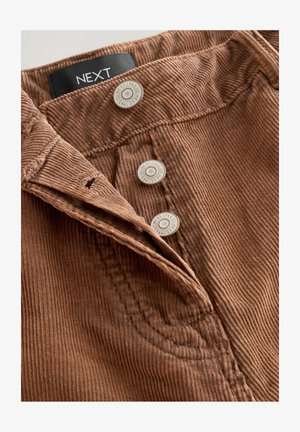 Brown corduroy fabric with vertical ridges, featuring a waistband and three silver buttons stamped with "NEXT 1982."