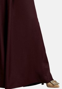Lang bordeauxrood jurk met een vloeiende silhouet. Kenmerkt zich door een gladde textuur en een zoom die de vloer beroert, gecombineerd met beige hakken versierd met een decoratieve gesp.