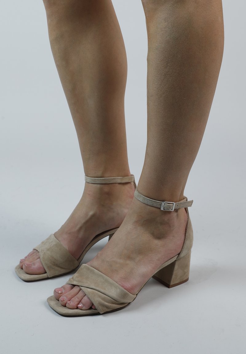 Beige suède sandalen met een blokhak, voorzien van een crisscross bandontwerp en een verstelbare enkelgesp voor een veilige pasvorm.