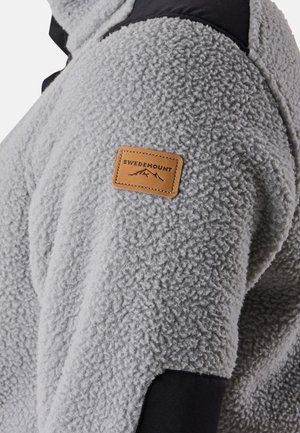 Gray fleece jacket with black shoulder accents. Features a leather tag labeled "SWEDEMOUNT" on the left arm. Soft texture, casual design.
