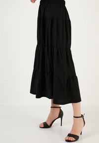 Black tiered maxi skirt with an elastic waistband, featuring a textured fabric. Paired with strappy black high-heeled sandals.