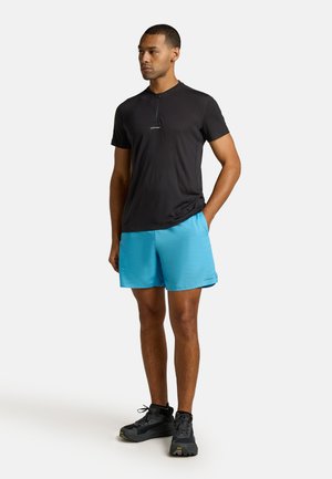 Zwarte korte mouwen zip-up shirt gecombineerd met felblauwe sportshorts en zwarte trailschoenen. Glad stof, relaxte pasvorm, geen opvallende patronen.
