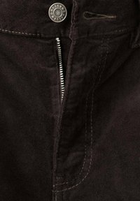 Zwarte suède broekdetail met een ritssluiting aan de voorkant, metalen knoop en contrasterende stiknaden. Gladde textuur met zichtbare naadtoespraken.