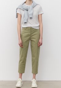 Lichtgrijze sweatshirt over een wit T-shirt, gecombineerd met hooggesneden, cropped olijfgroene broeken en witte sneakers.