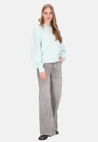 Licht muntgroene trui met oversized mouwen, gecombineerd met grijze wijde jeans en zwarte schoenen. Eenvoudig, casual design.