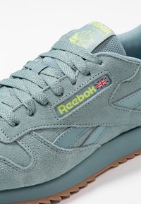 Reebok sneakers i ljus blågrön mocka, med en texturerad ovandel, platta snören, gul logotyp och en brun gummisula.