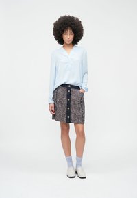 Svetlomodrá košeľa s golierom a dlhými rukávmi s voľným strihom, doplnená o textúrovanú viacfarebnú sukňu po kolená s veľkými gombíkmi a námorníckym pásom.