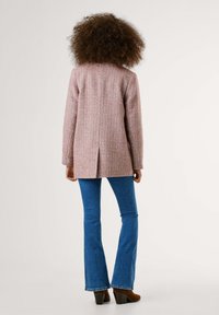 Blazer en vichy rose avec manches longues, fente simple à l'arrière, associé à un jean bleu évasé et des bottes marron à talons.