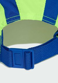 La gorra ajustable presenta una tela verde brillante y azul, una correa de nailon texturizada y una hebilla de plástico azul con una superficie decorada.