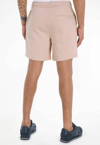 Pantalones cortos rosa claro hechos de una suave mezcla de algodón, con una cinturilla elástica y un solo bolsillo trasero. Llevados con zapatillas oscuras.
