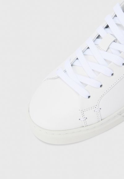 Λευκό δερμάτινο αθλητικό παπούτσι με επίπεδα λευκά κορδόνια, στρογγυλερή μύτη και λαστιχένια σόλα. Διαθέτει διακριτική ραφή κατά μήκος των πλευρών. Μινιμαλιστικός σχεδιασμός.