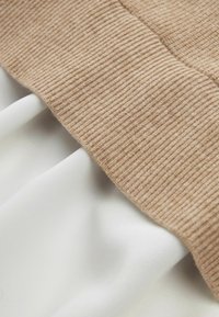 Le tissu côtelé beige en haut se transforme en un tissu blanc doux en dessous, mettant en valeur des textures contrastées et un drapé lisse.