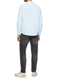 Lichtblauw overhemd met lange mouwen en een knoopkraag, gecombineerd met donkergrijze jeans en witte sneakers. Glad materiaal, casual pasvorm.