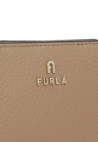 Portafoglio in pelle tessurizzata di un beige chiaro, con il logo dorato "FURLA" in mostra. Bordature cucite e finitura liscia.