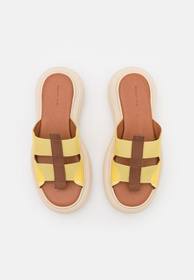 Chinelos amarelos com detalhes em têxtil castanho nas tiras e uma sola bege. Palmilha de couro lisa com uma forma arredondada.