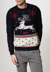 Marinblå tröja med ett vitt rendesign, röda och vita geometriska mönster samt en ribbad krage och nederkant.