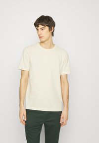 Lys beige kortærmet t-shirt med rund halsudskæring, glat tekstur og en afslappet pasform, kombineret med mørkegrønne bukser.